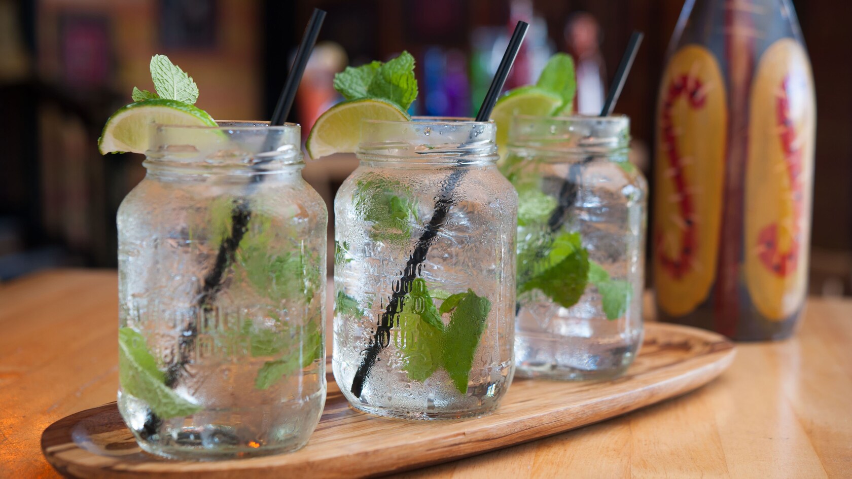 Trois mojitos en pots Mason, garnis de lime et de menthe, sur un plateau en bois de forme oblongue