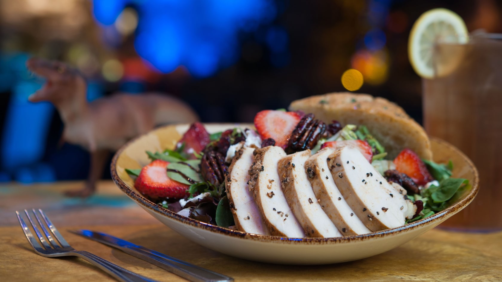 Una ensalada con pollo cortado, lechuga, queso de cabra, fresas, cebollas y nueces pecanas