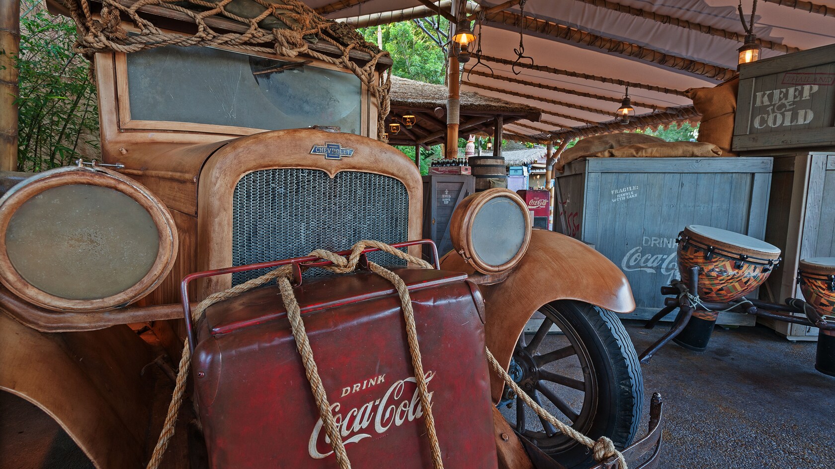 Antique car with netting on its roof, Coca-Cola® cooler tied to its front and drums in the background