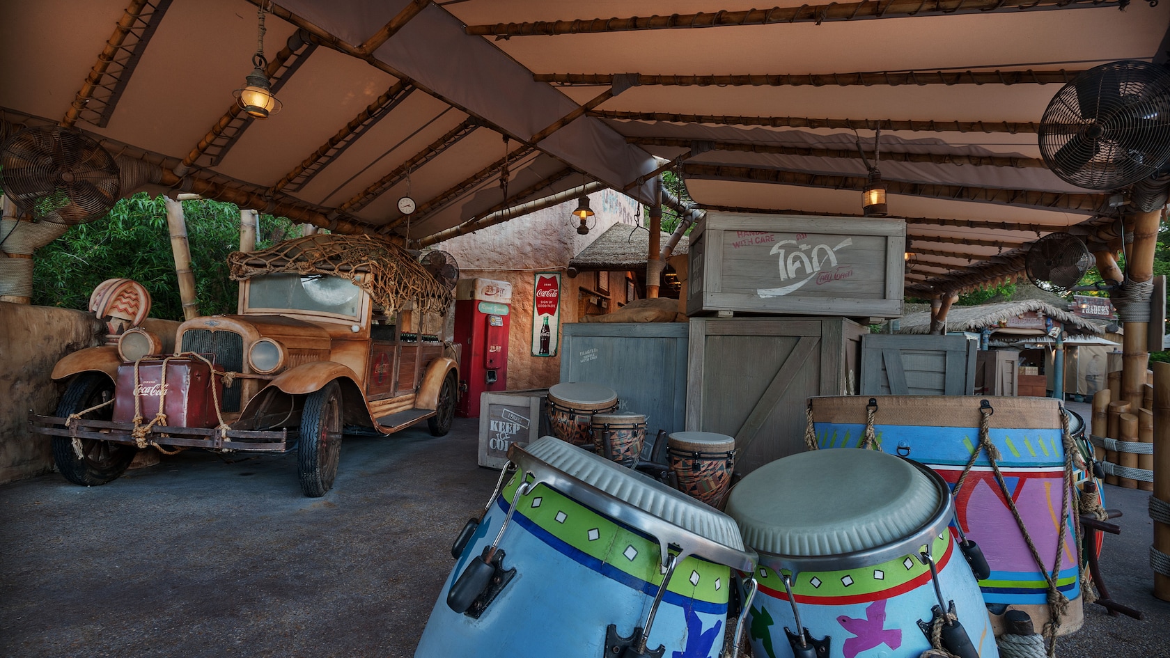 African drums in the foreground with crates, antique car and Coca-Cola® signs under the awning