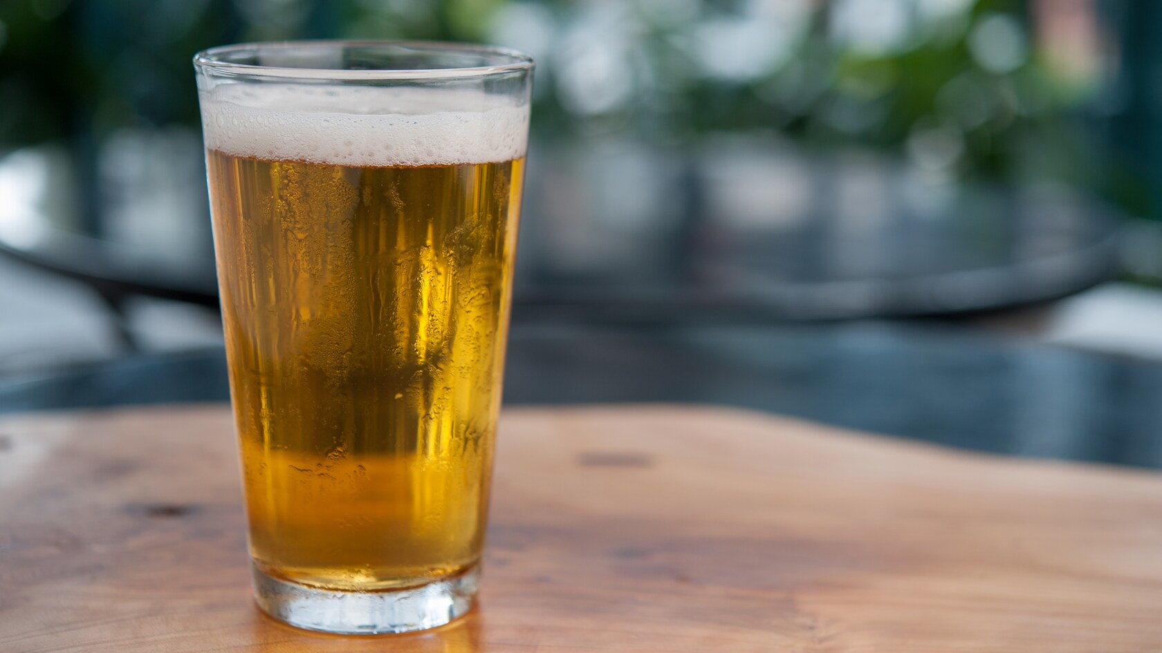 A plastic cup filled with frosty, frothy ale, served atop a wooden outdoor table