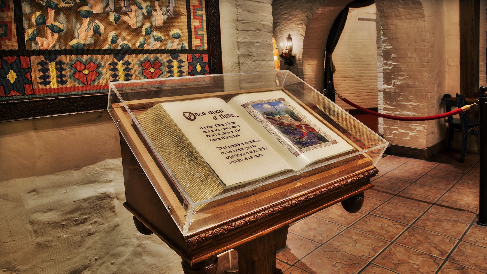 An open storybook with gold-leaf pages inside a Plexiglas case on a podium