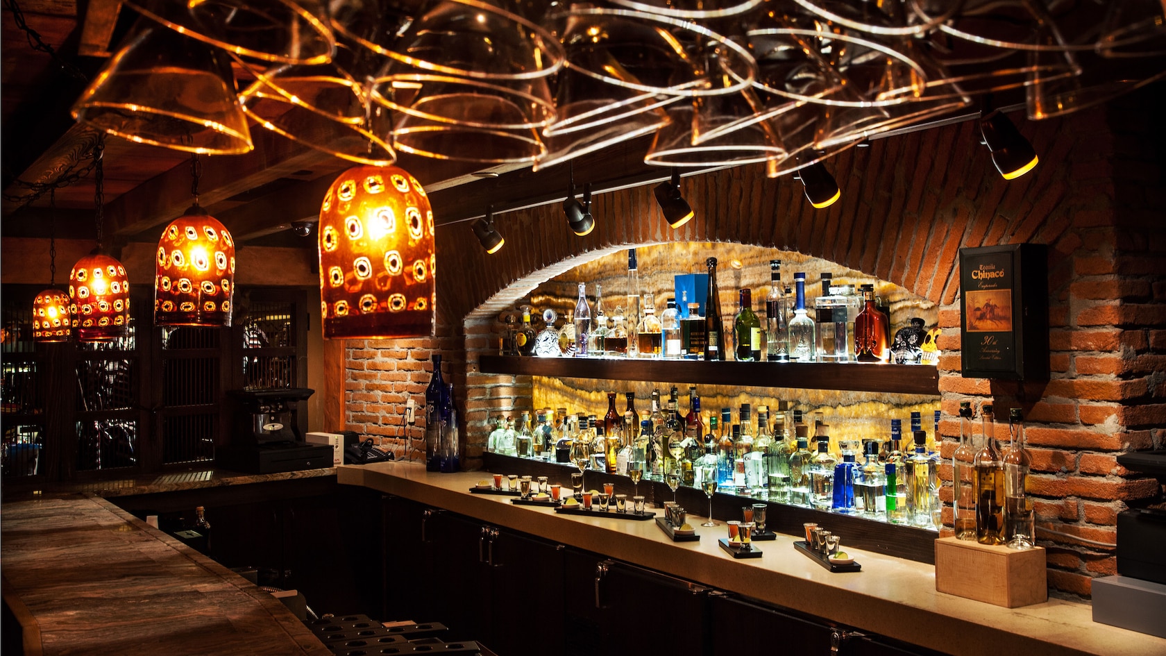 Liquor bottles on shelves inside a brick alcove with overhead lights  
