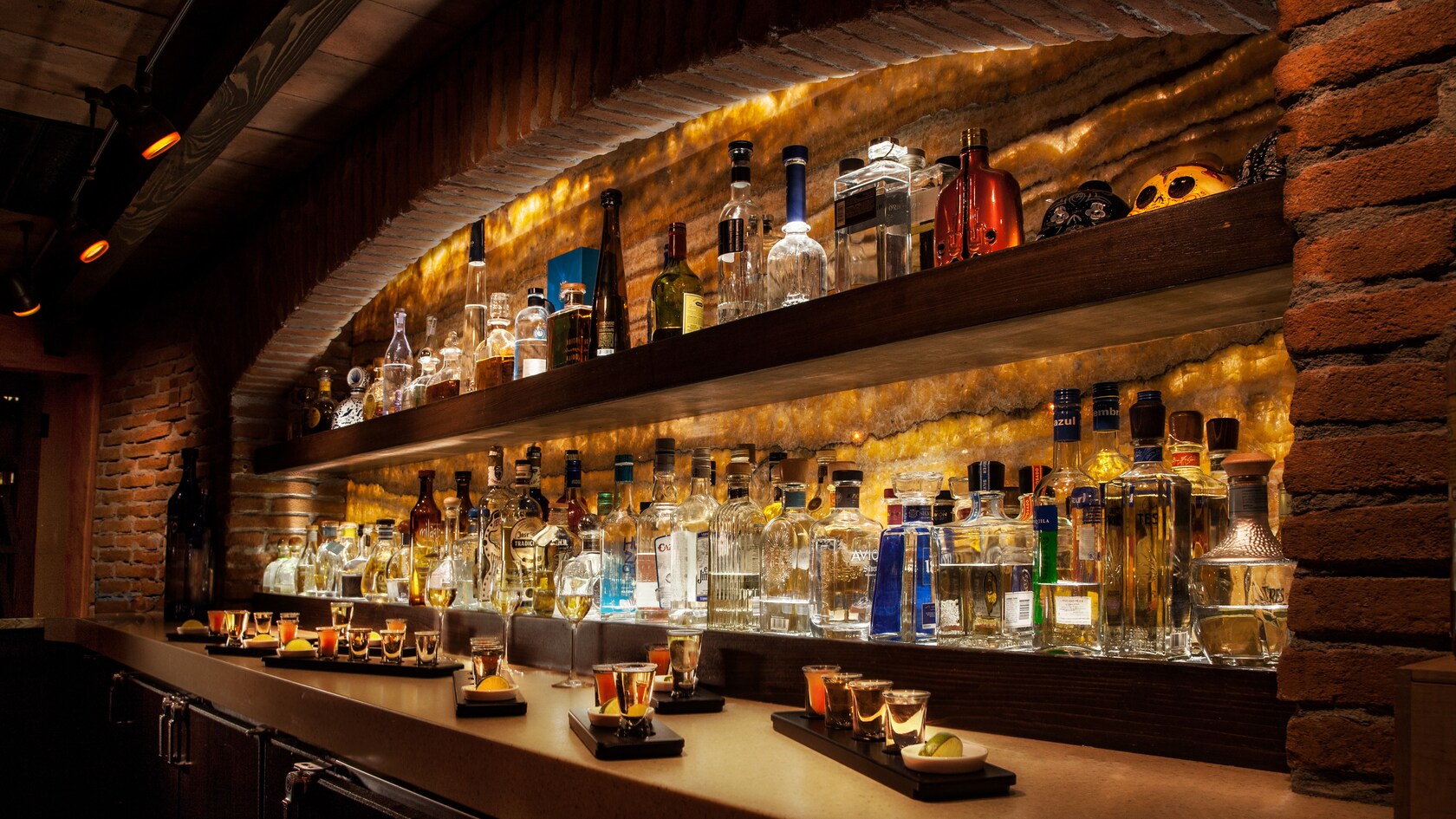 Shelves holding bottles of liquor with small trays holding shot glasses of tequila