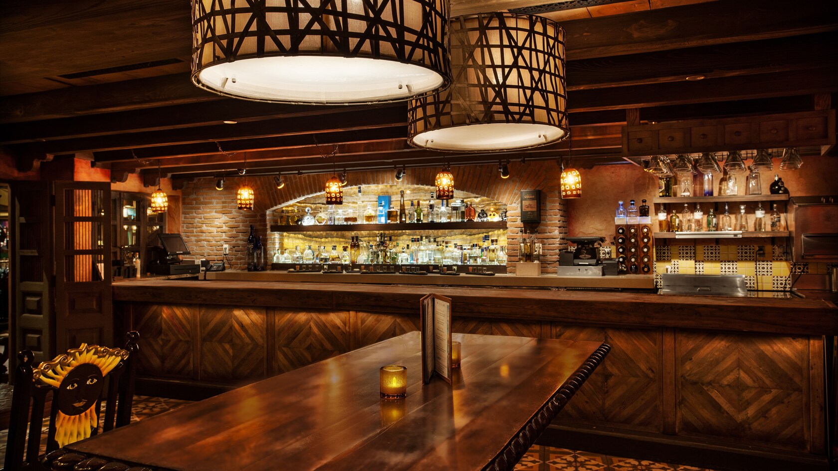Dining table and chair, overhead lights and bar in the background
