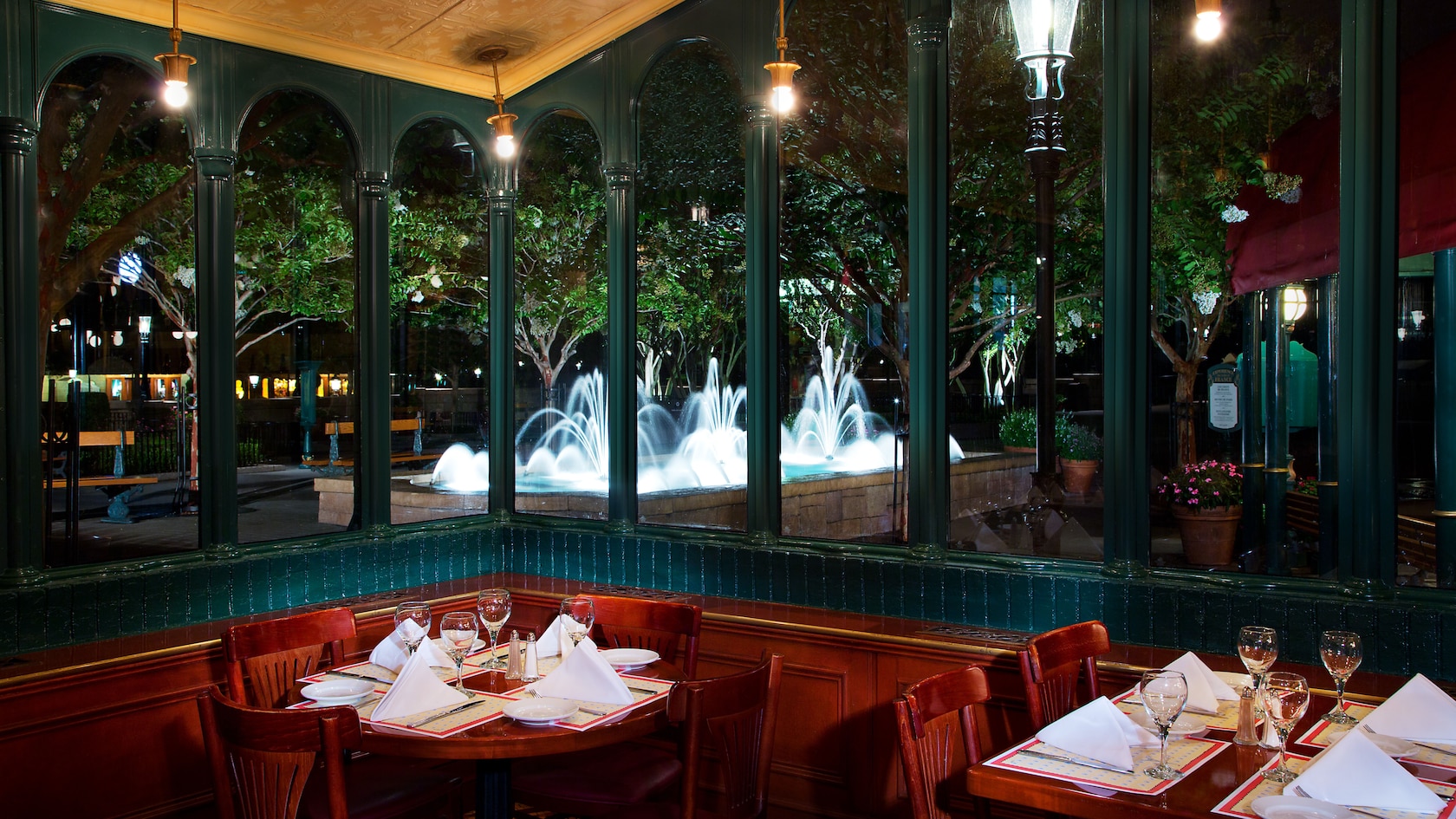 Two tables next to windows with view of a lit-up outdoor fountain at Chefs de France at night