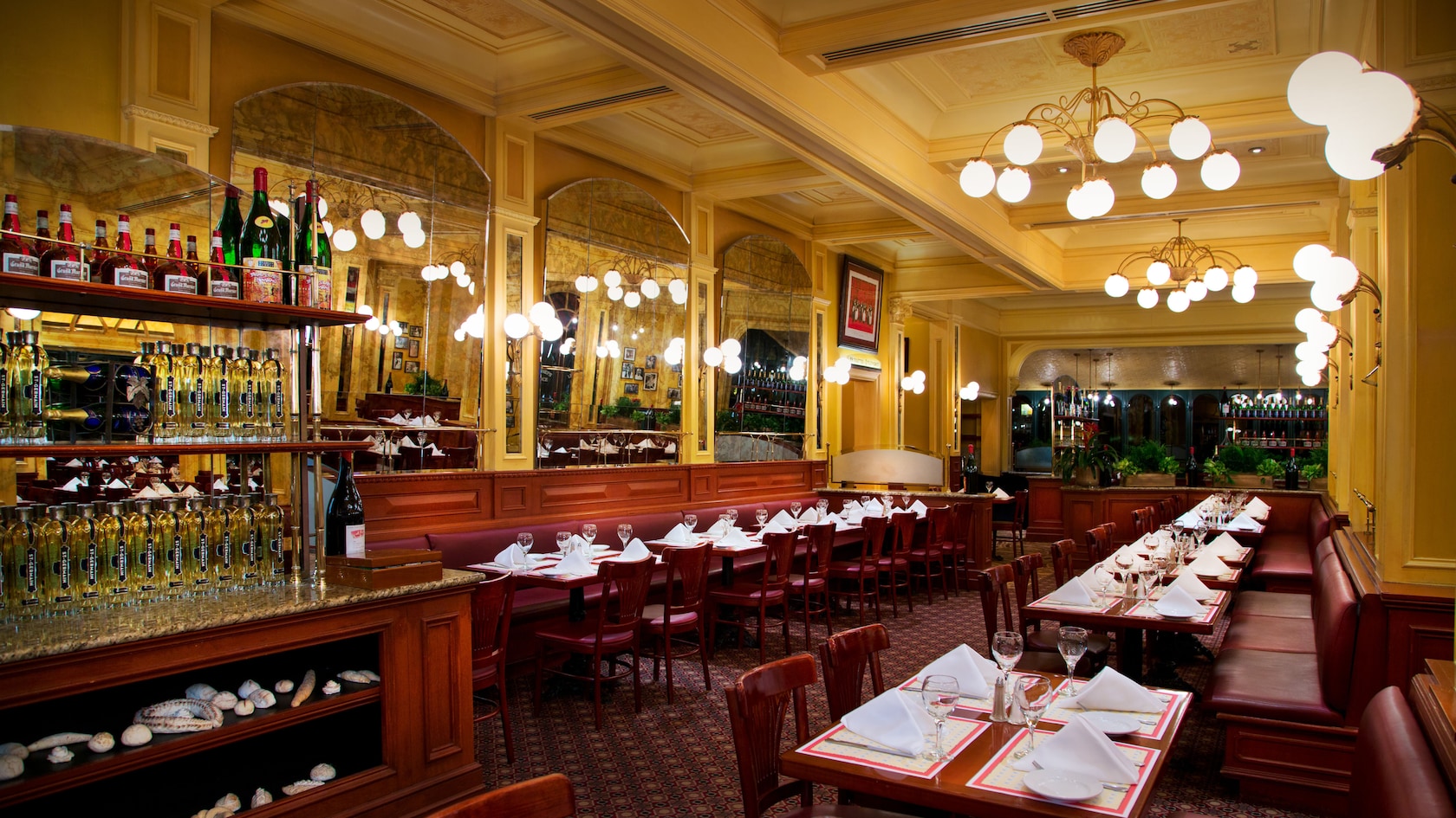 Dining area with banquette seating, 2 chandeliers and a wall with 3 large panel mirrors