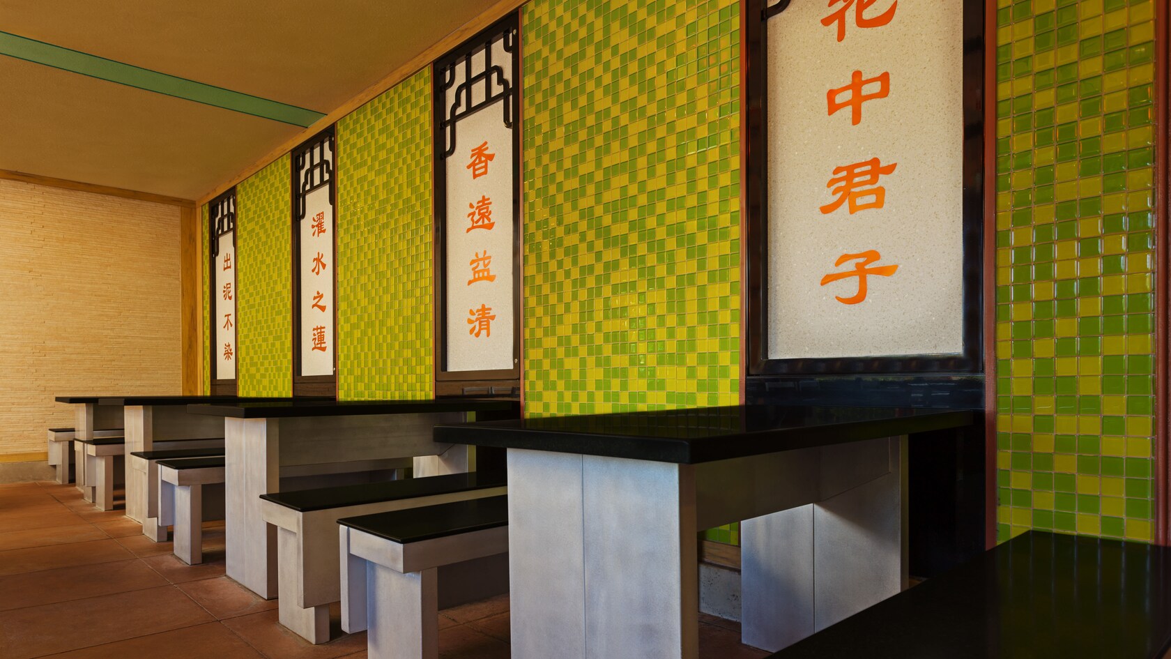 Dining area with tables and benches next to wall panels with decorative Chinese writing