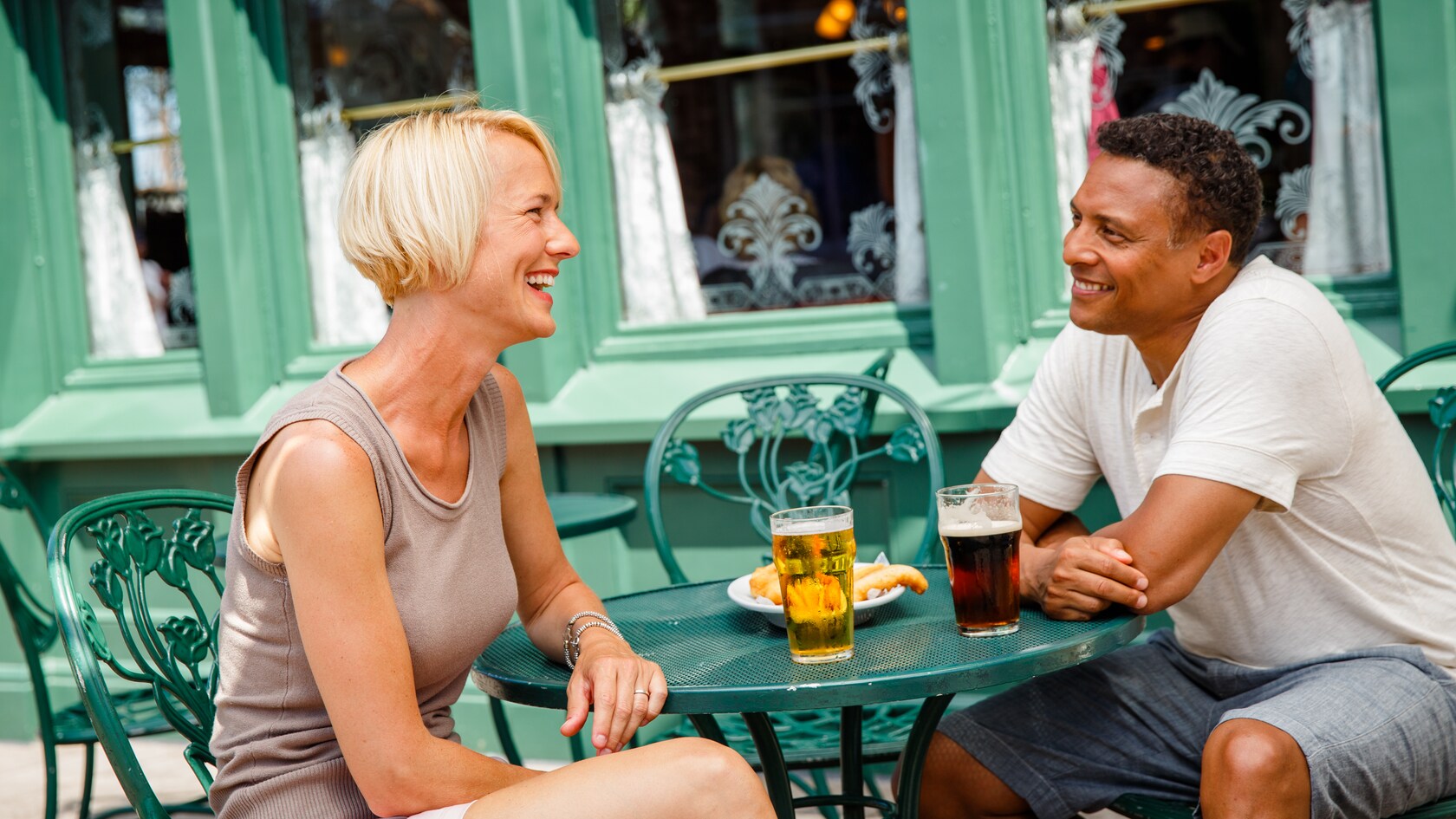Una pareja sentada en una mesa del patio con dos vasos de cerveza y pescado con papas fritas.