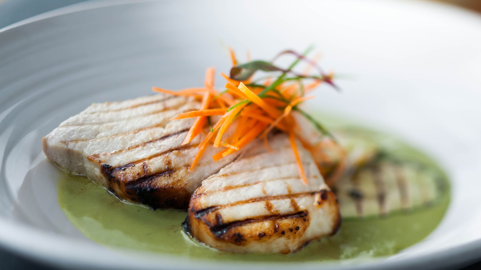 Tres trozos de pescado wahu y zanahorias cortadas en Juliana con salsa cremosa pueblano