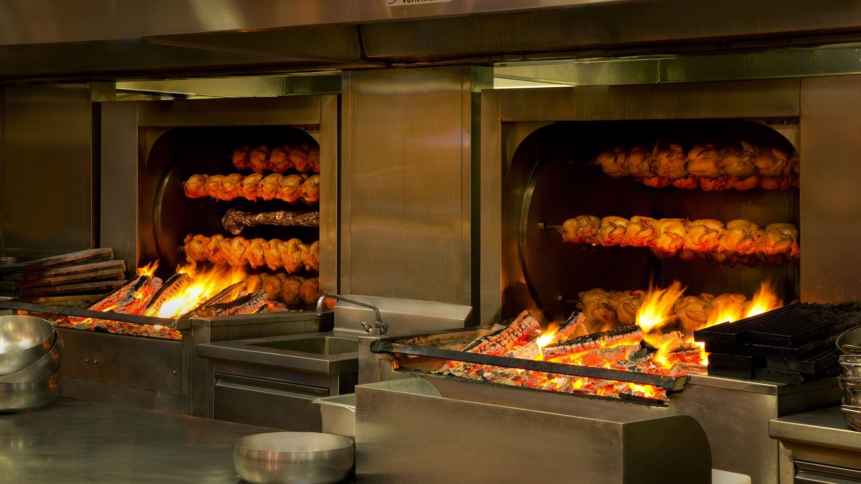 Dos hornos asadores gigantes a leña con filas de pollos cocinándose