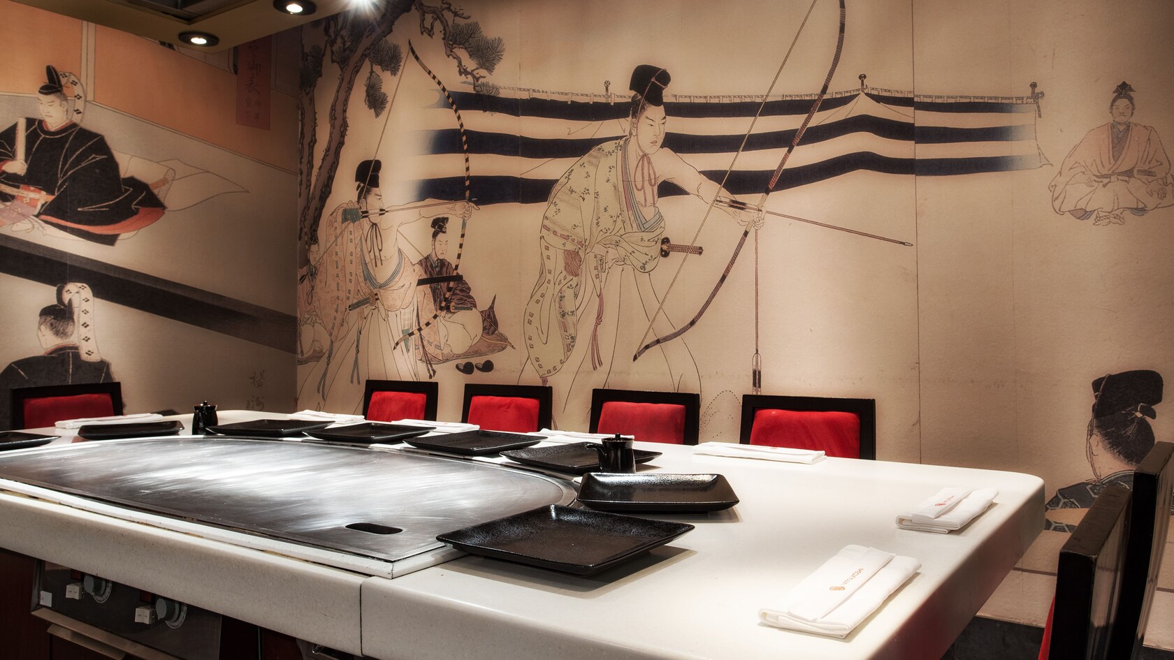 Un mural japonés del período Edo que muestra arqueros sobre la pared detrás de una mesa 