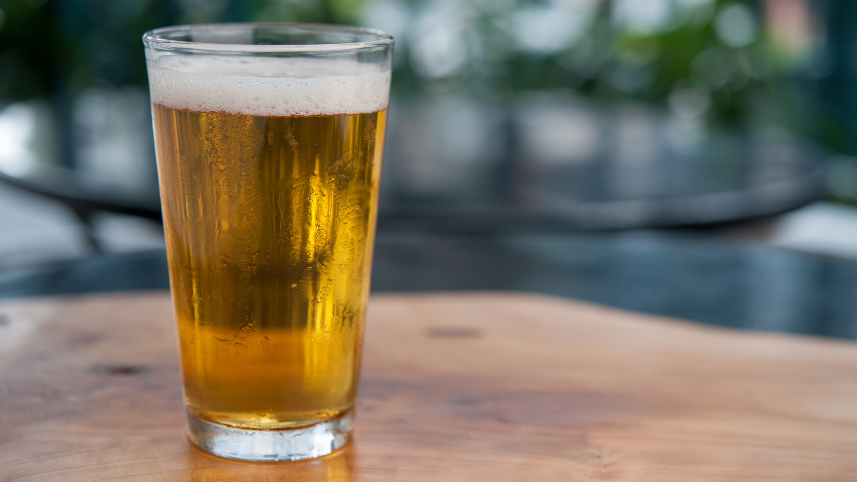 A pint of frosty, frothy ale served inside a classic pub glass and set atop a wooden outdoor table