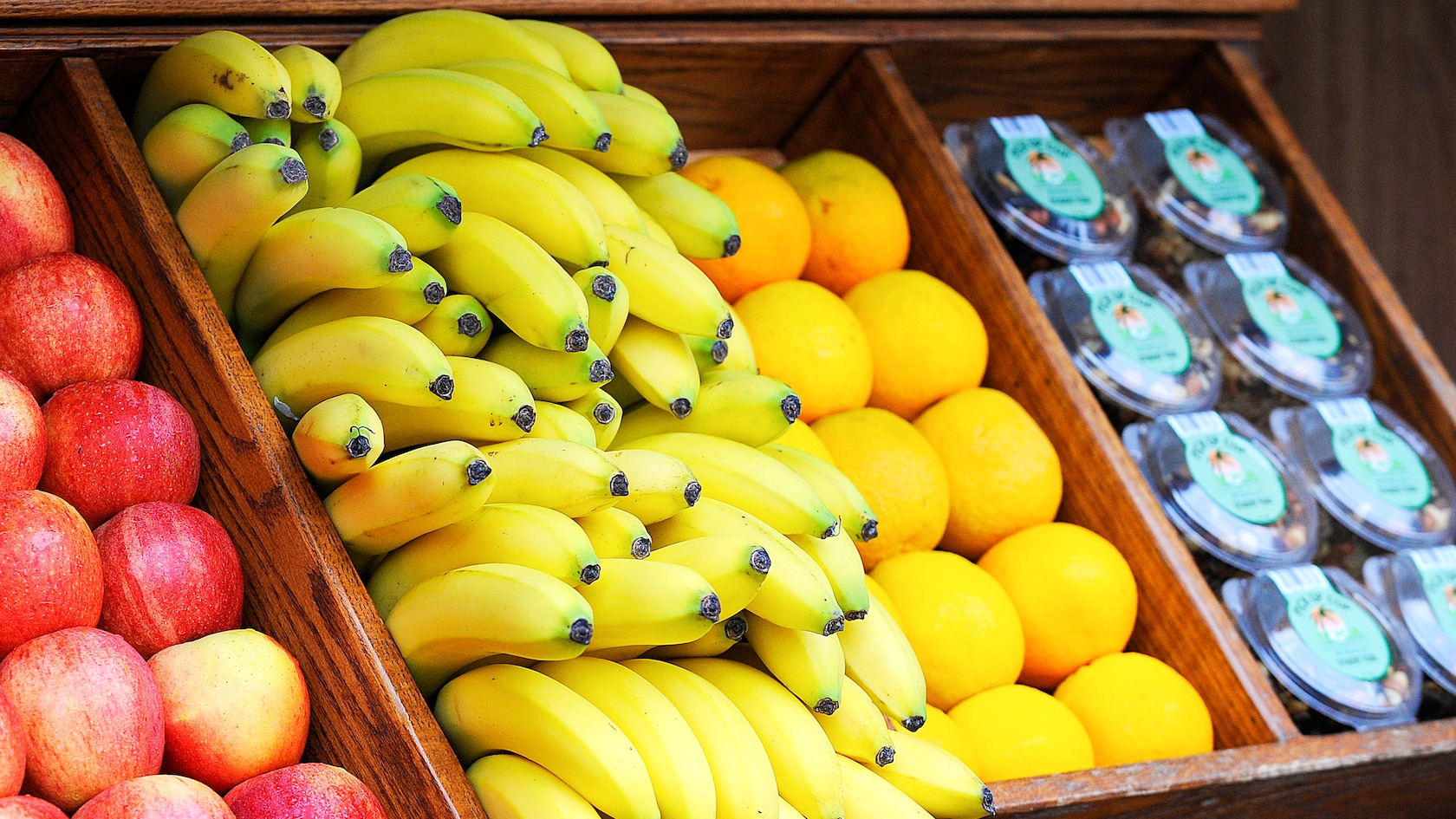 Apples, bananas, oranges and containers of trail mix on display within wooden crates