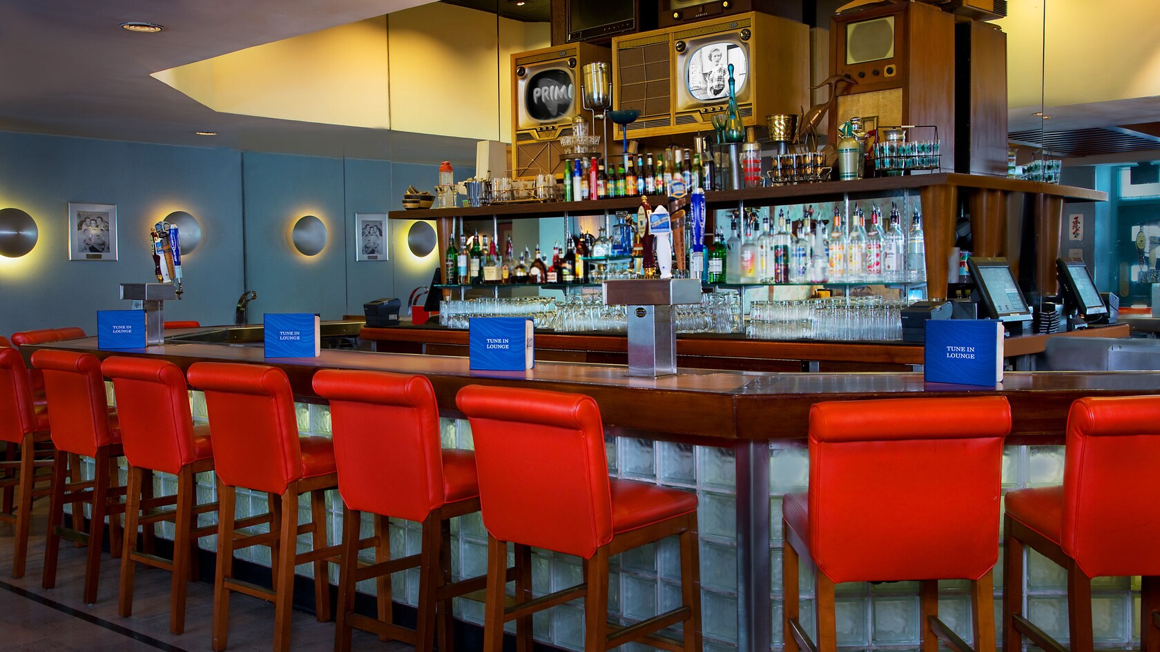 Stool-chairs at a wooden bar and an old TV above shelves with liquor bottles 