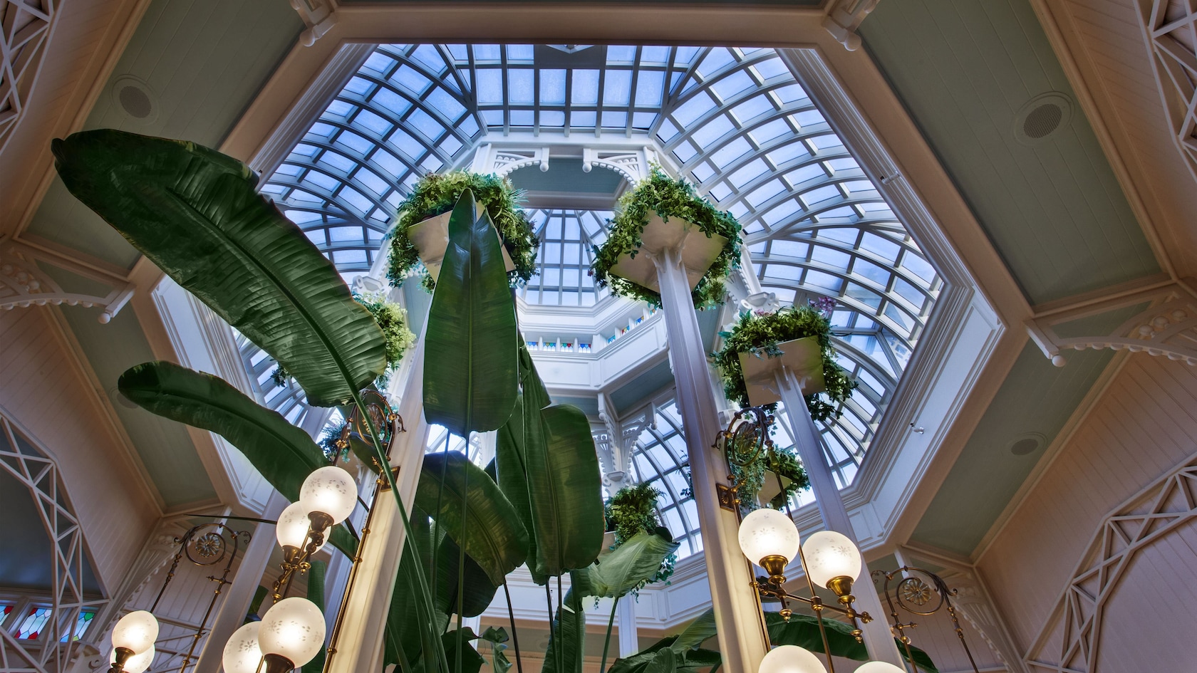 View looking up at a domed glass ceiling and several hanging plants atop tall pillars