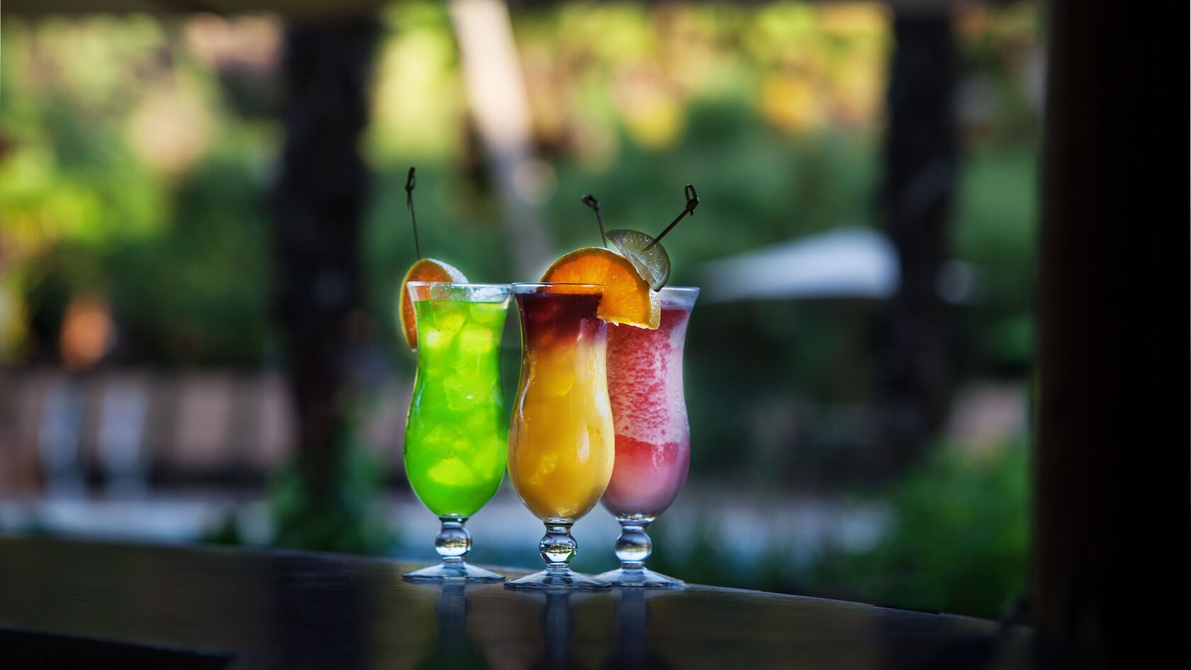 Three specialty drinks sitting on a wooden bar