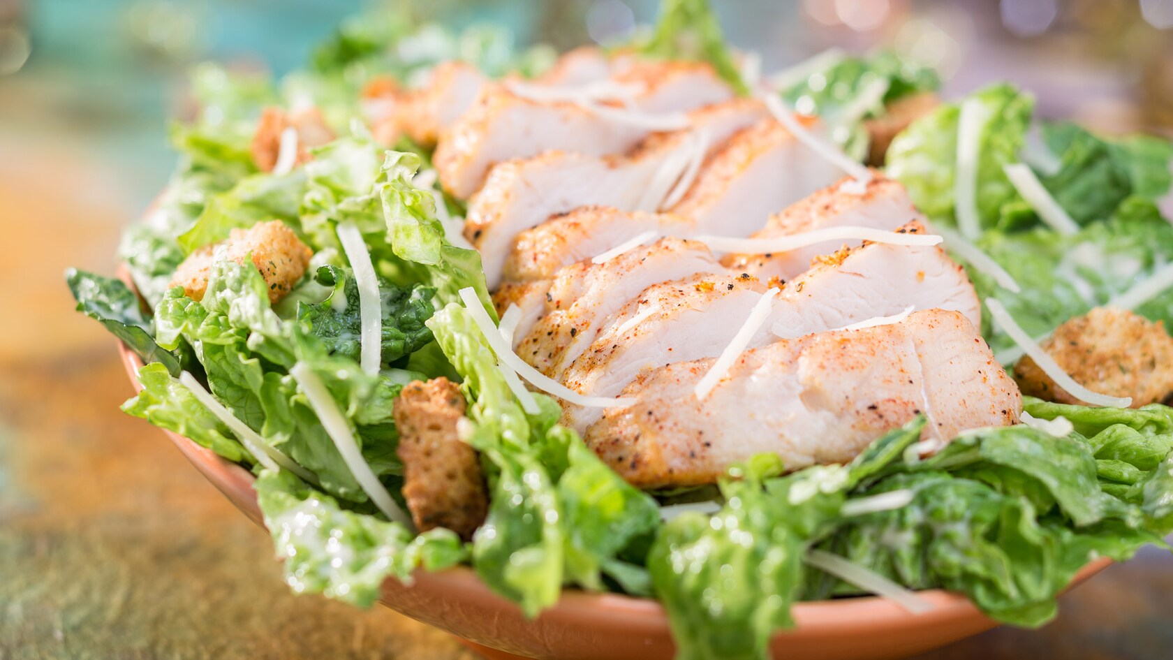 Pechuga de pollo en rodajas espolvoreada con queso rallado sobre una cama de lechuga con crutones