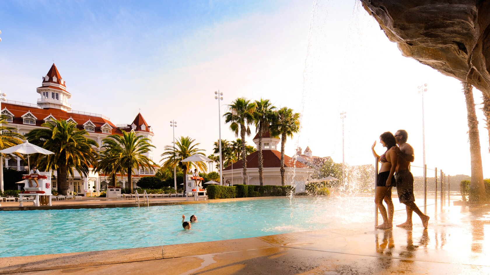 A mom and dad wave to their children swimming in the pool at Disney's Grand Floridian Resort & Spa