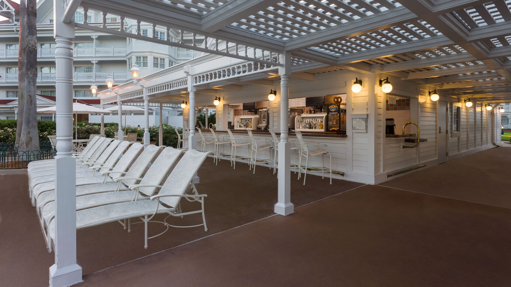 A row of deck chairs sit next to a poolside bar with the hotel in the background