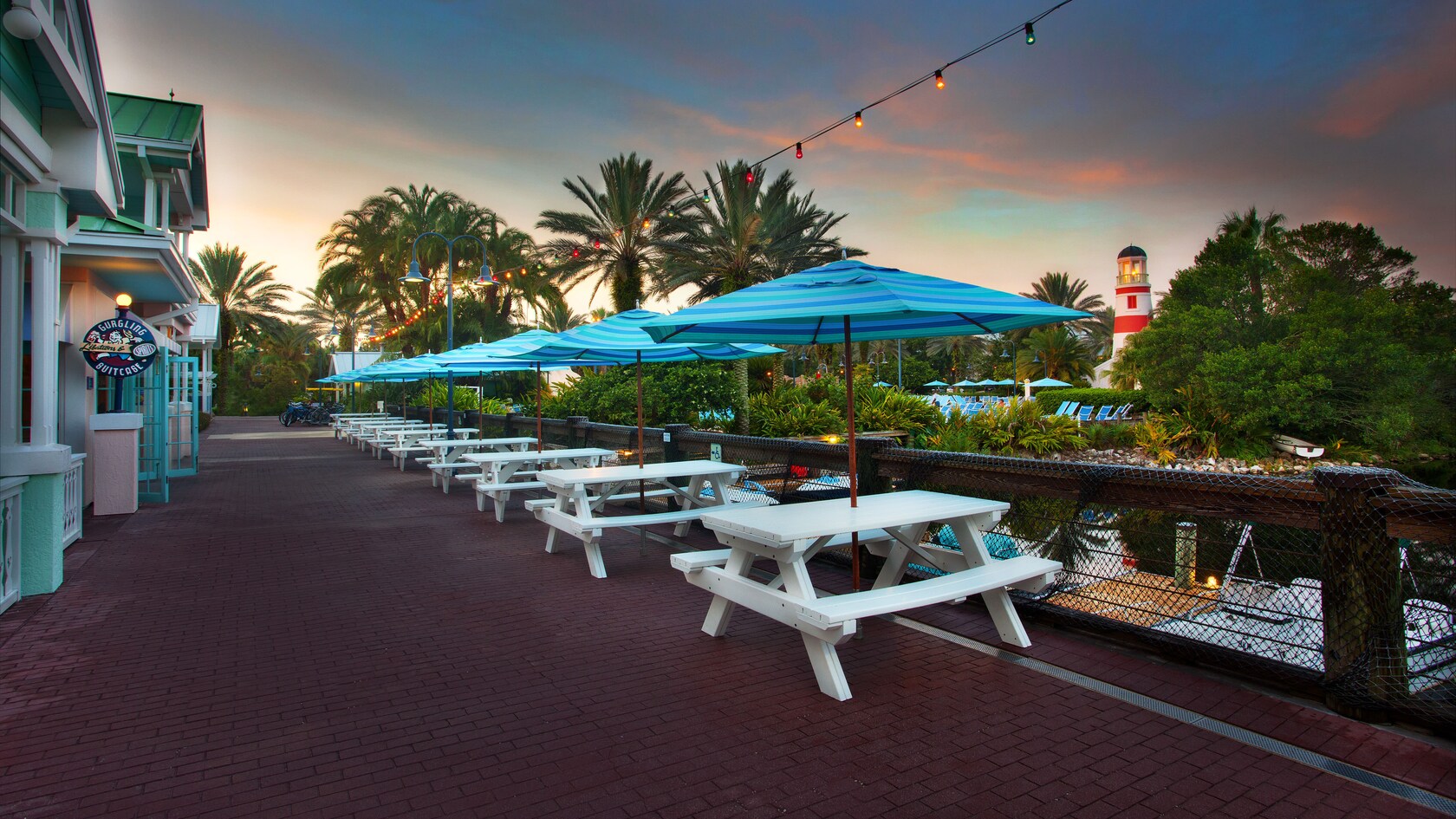 Row of white picnic tables and blue umbrellas