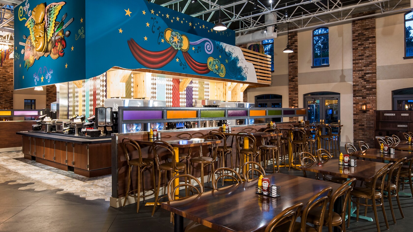 Un área de comidas amplia, con mesas y sillas de madera, y un mural con temática de Mardi Gras