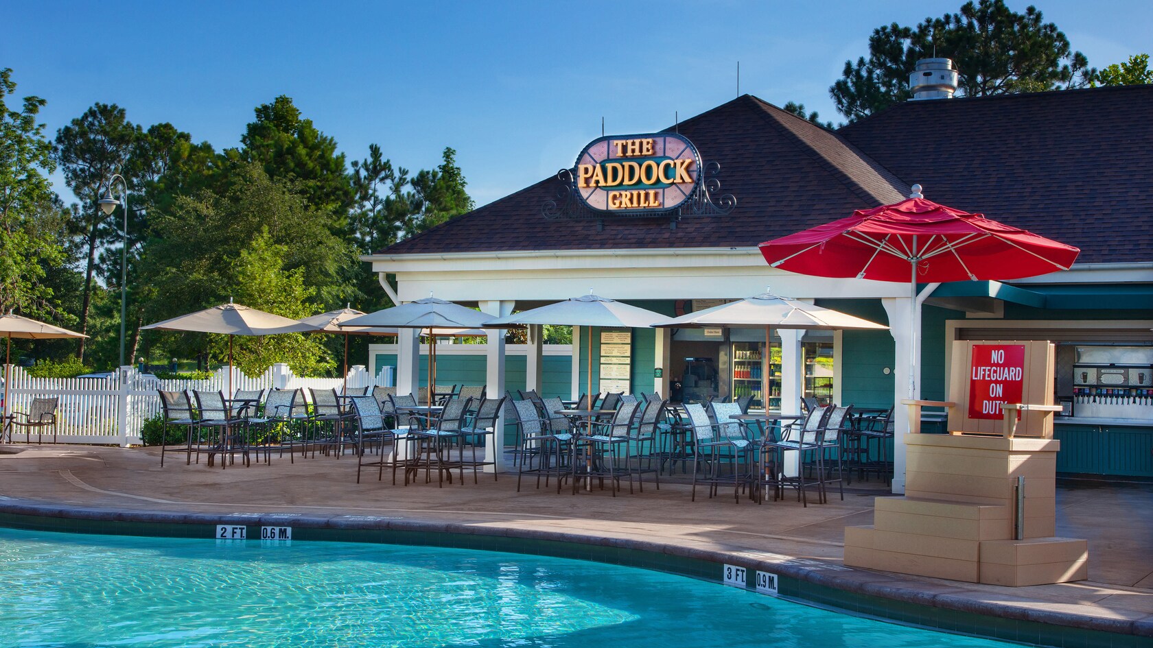 View of The Paddock Grill, patio tables and lifeguard chair from across the Paddock Pool