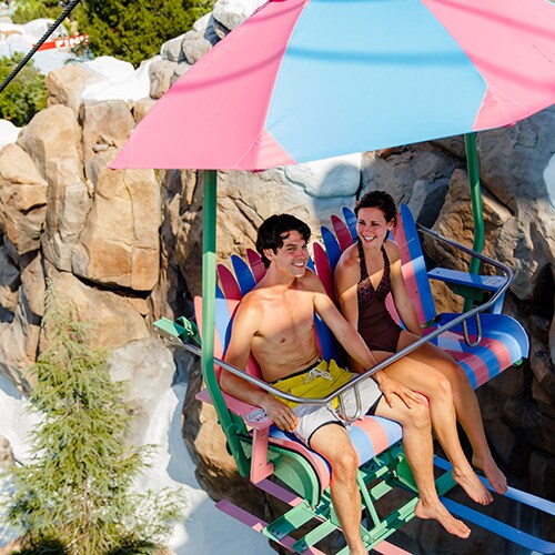 A teenaged boy and girl ride the colorful chairlift up Mount Gushmore at Disney's Blizzard Beach