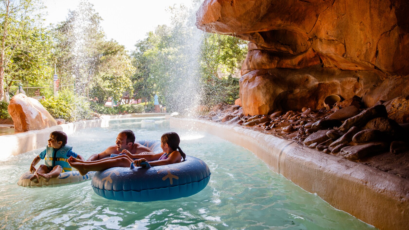 Three Guests riding inner tubes through a gentle waterfall at Cross Country Creek in Disney’s Blizzard Beach water park