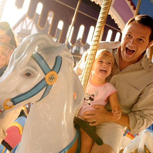 A dad holds his young daughter while riding a horse on Prince Charming Regal Carrousel