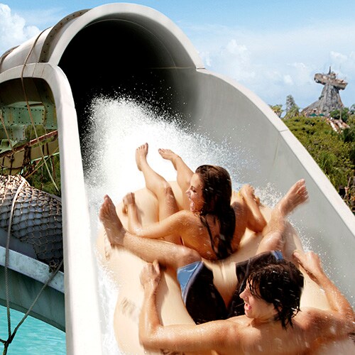 A couple sharing a raft slide backwards down Crush 'n' Gusher water coaster