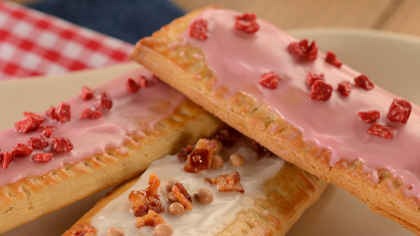Pastries topped in frosting, bacon and candy resting on a plate and a tablecloth