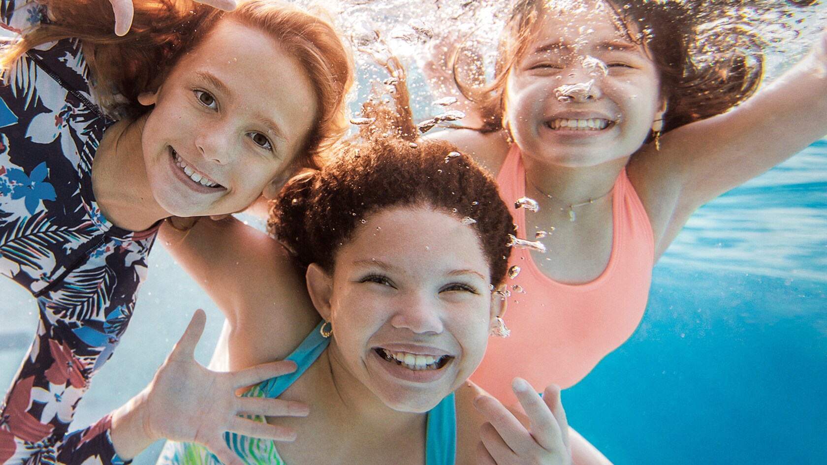 Three girls smiling underwater while swimming in a pool at a Walt Disney World Good Neighbor Hotel