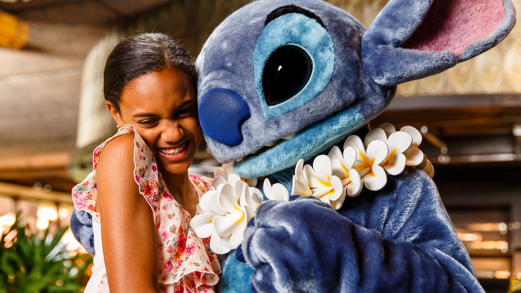 A girl smiles while giving Stitch a hug