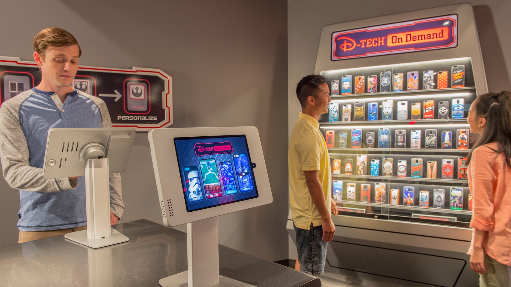 A young man operates a touch screen while a teen boy and girl look at a display offering a selection of computer games