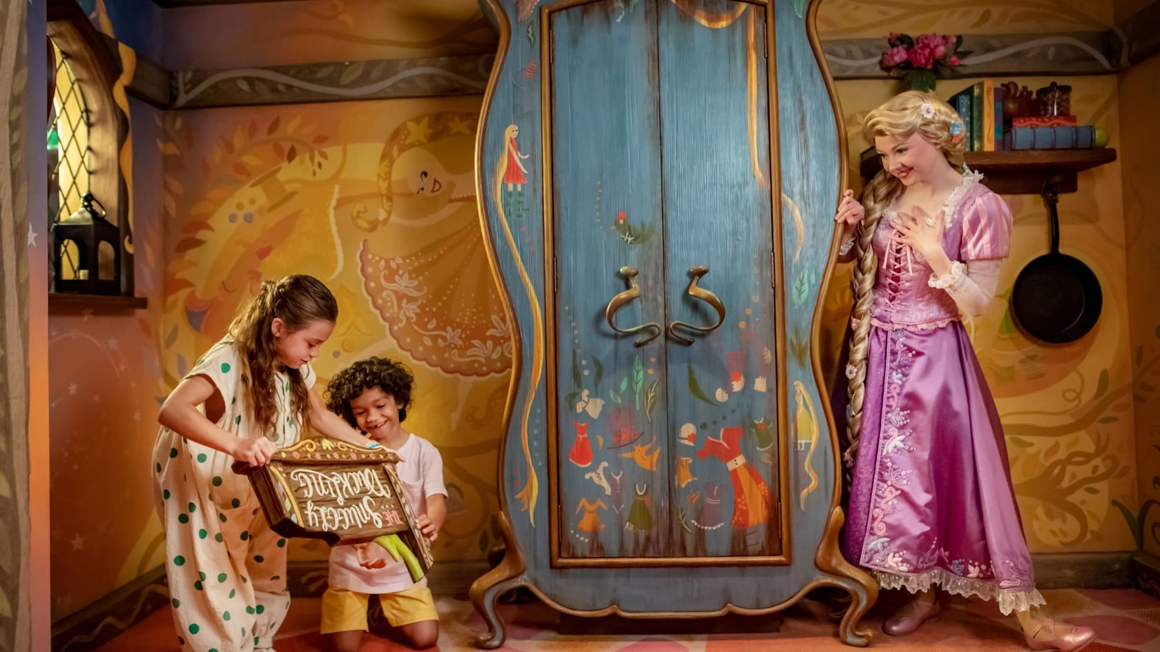 Rapunzel peeking around an armoire at 2 small children playing in a fanciful storybook setting