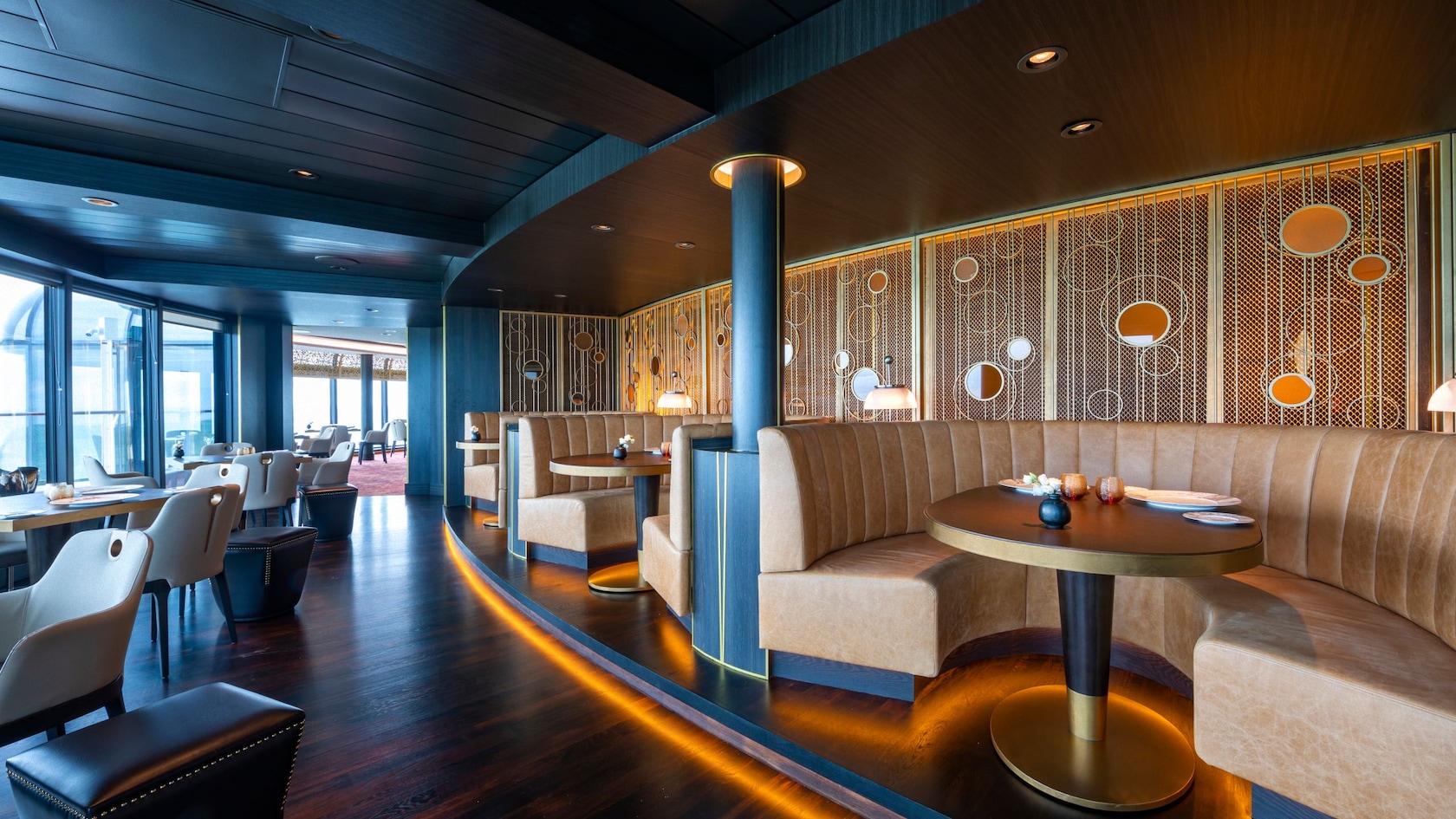 A modern steakhouse setting with ocean views, circular leather booths and contemporary tables and chairs