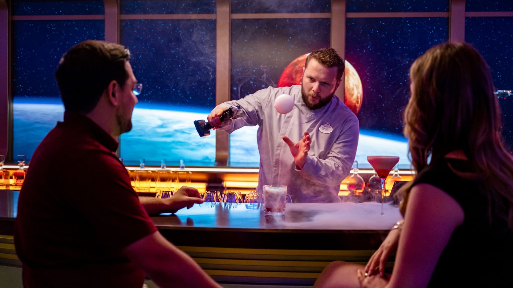 A bartender performing a bar trick with a small floating orb for 2 guests in the Star Wars Hyperspace Lounge