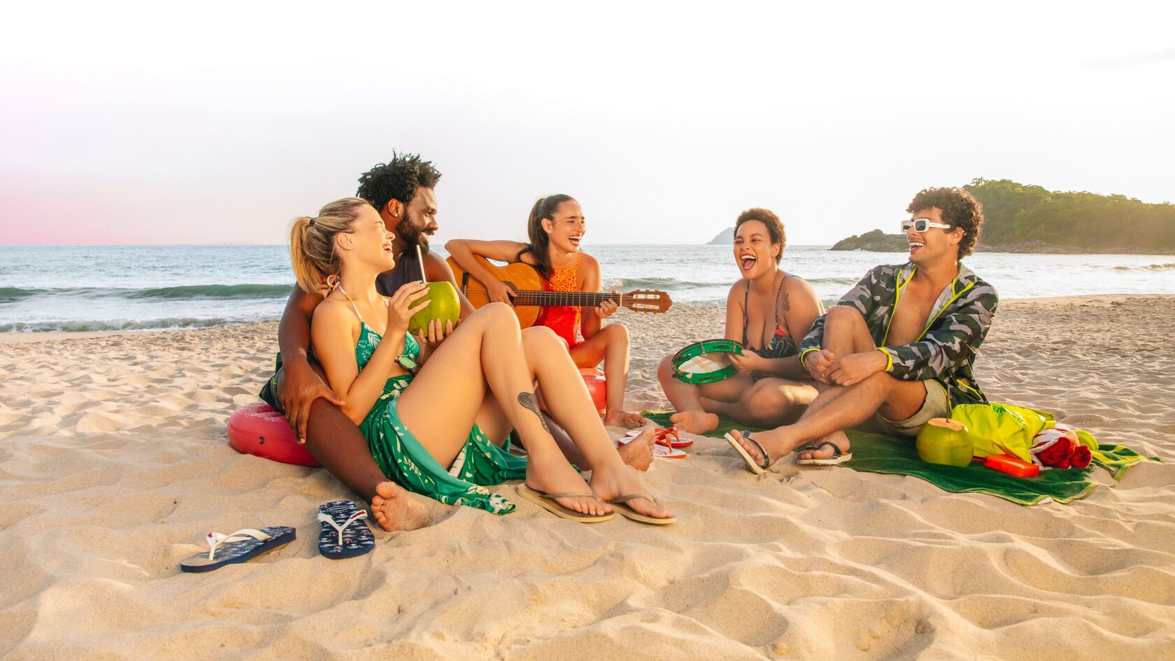 A group of friends sit in a circle on the beach, talking and laughing