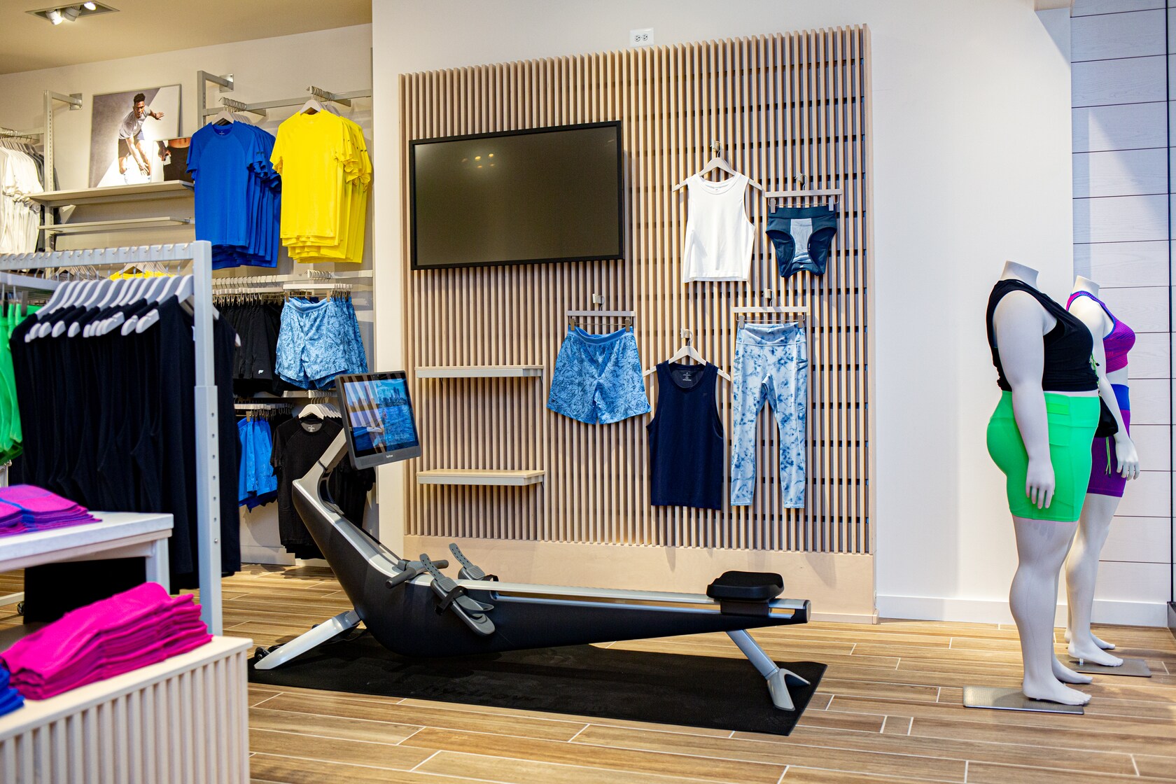 El interior de una tienda de Fabletics, con una máquina de remo, 2 maniquíes con ropa deportiva y estantes repletos de ropa deportiva
