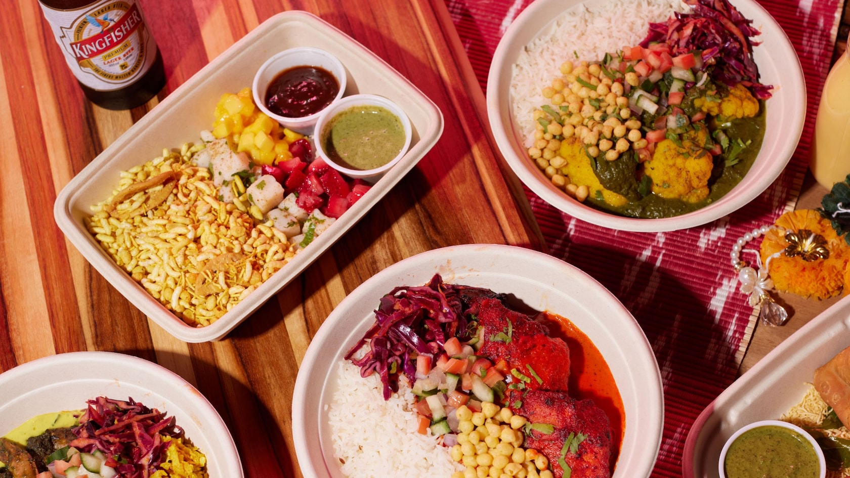 A bottle of lager next to several containers of Indian inspired meals