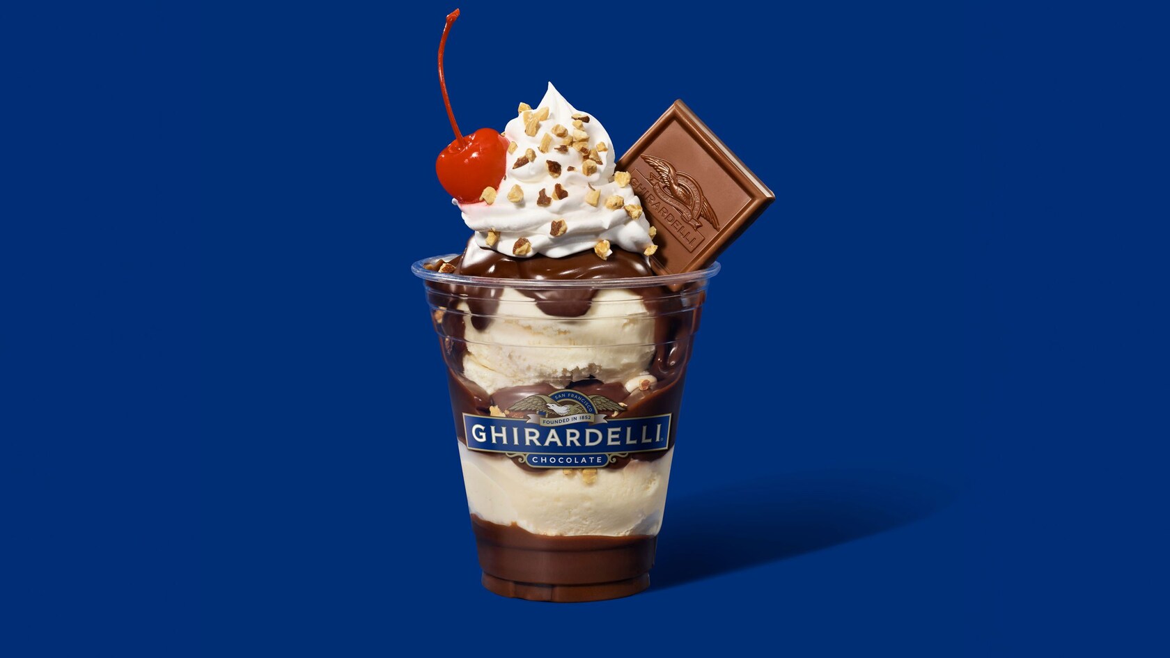 Helado de vainilla cubierto con salsa de chocolate caliente, crema batida, almendra picada, una cereza y un cuadrado de chocolate