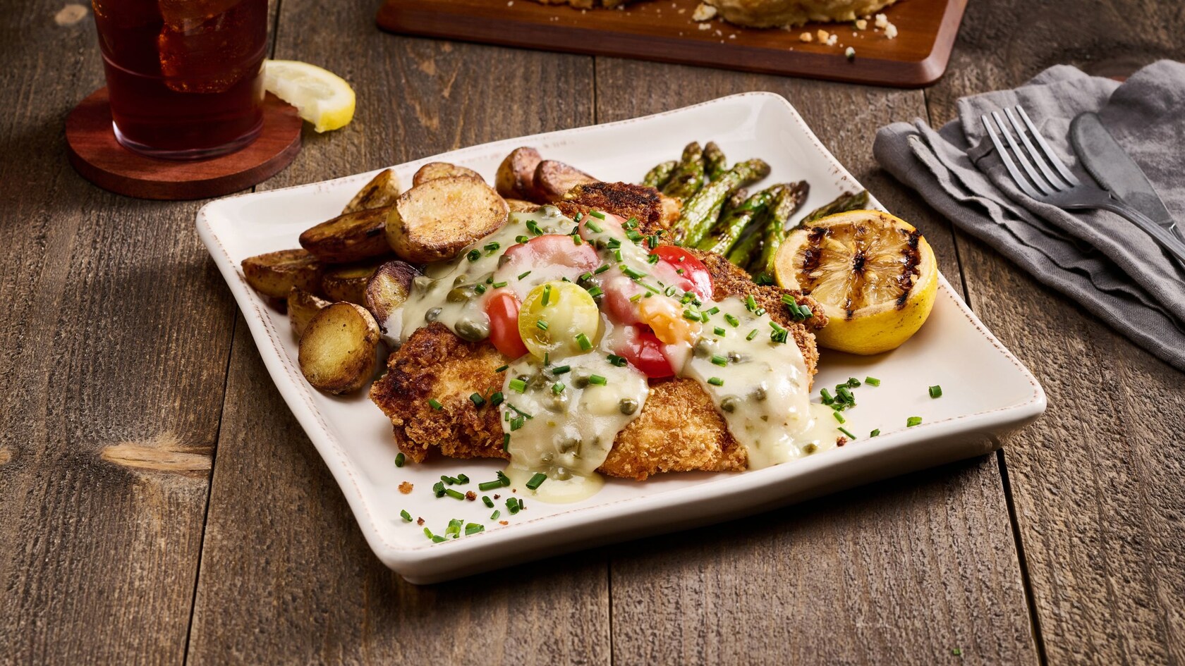 A dinner platter with a fried chicken cutlet topped with garlic, caper and gravy, served with potatoes and asparagus