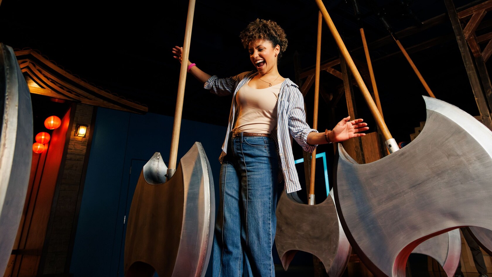 A young woman laughing while navigating between large swinging axe like pendulums in a darkened challenge room