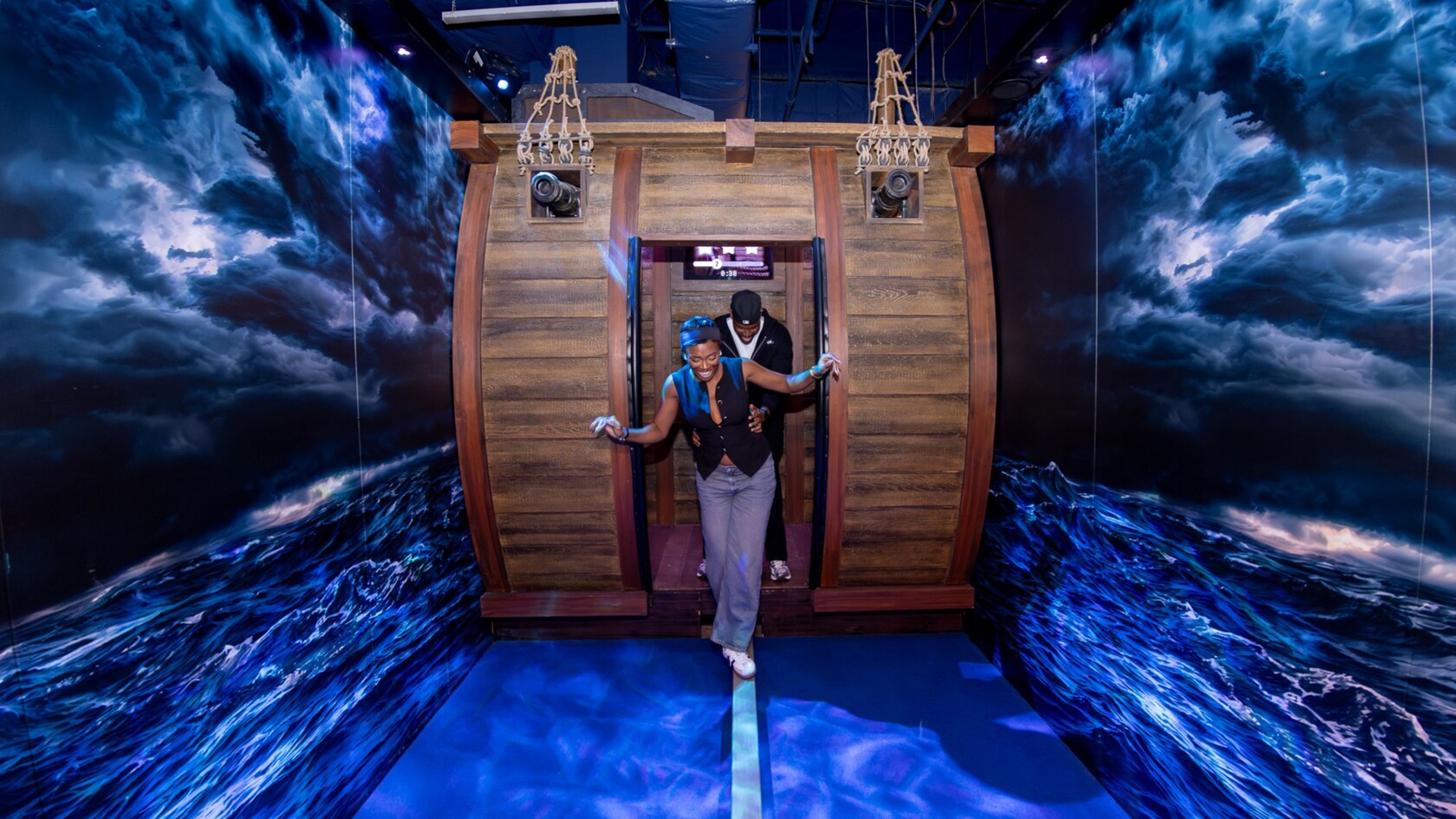 2 Guests laughing as they exit a nautical themed challenge room surrounded by ocean wave murals