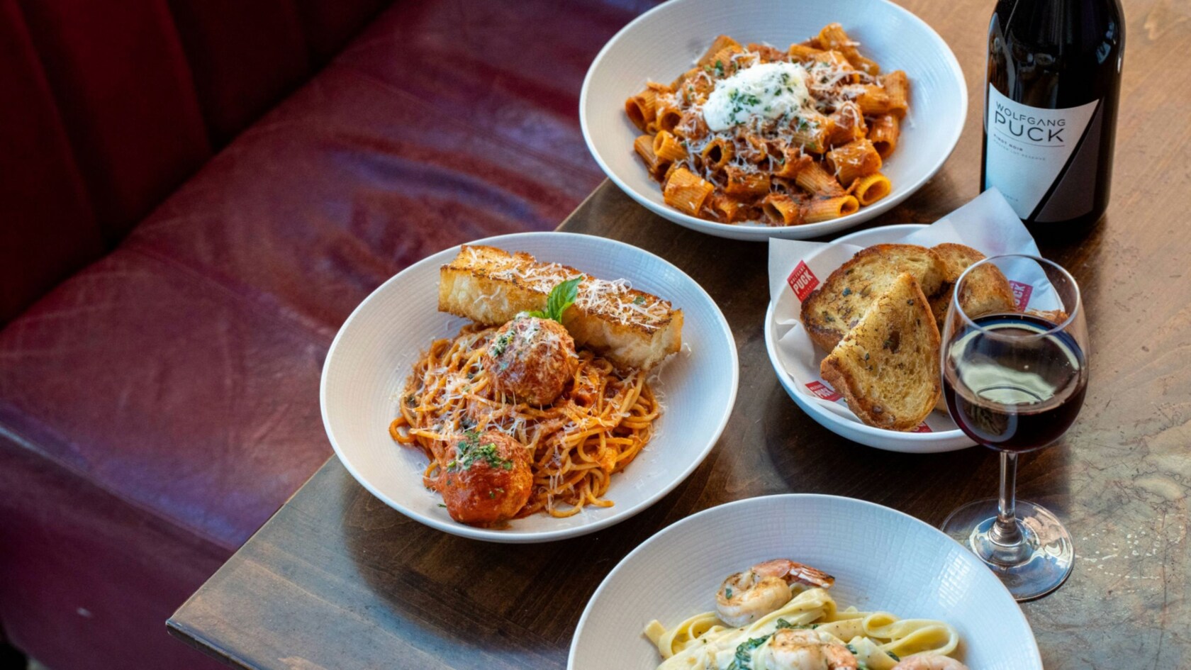 Three bowls of pasts, a bowl of bread, a glass of wine and a wine bottle