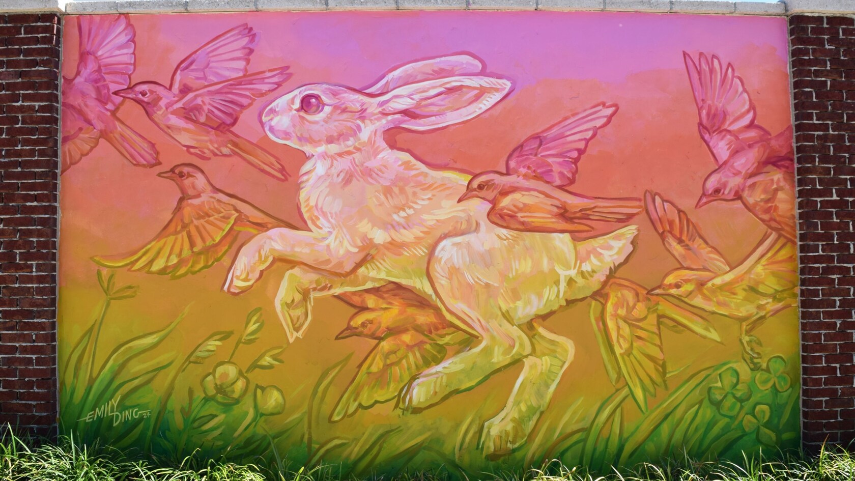 Un mural sobre una pared de ladrillo de la artista Emily Ding con un conejo rodeado de aves, sobre un fondo degradado