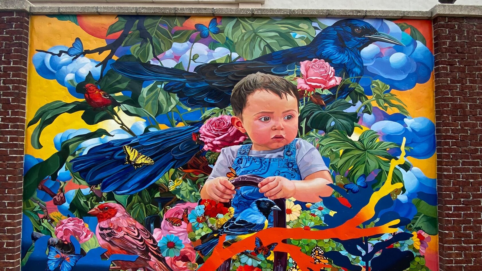Un mural de un niño pequeño sentado entre vida vegetal, aves y mariposas