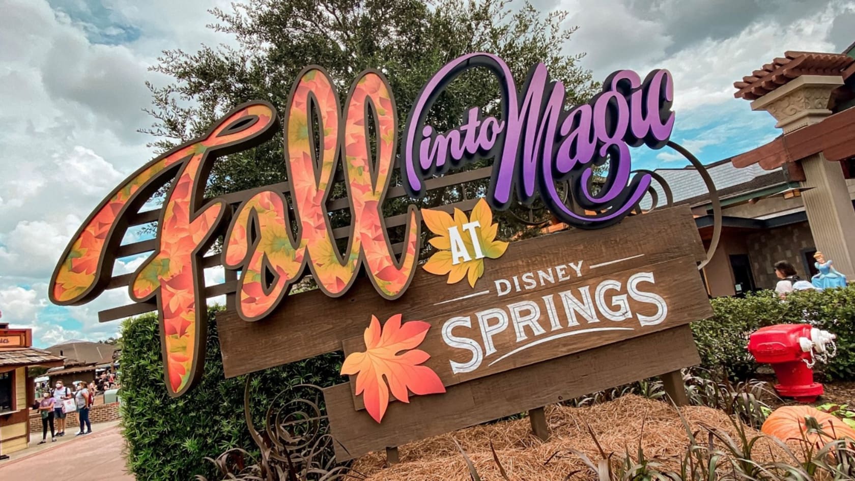A sign decorated with leaves in front of Disney Springs reads ‘Fall into the Magic’ 