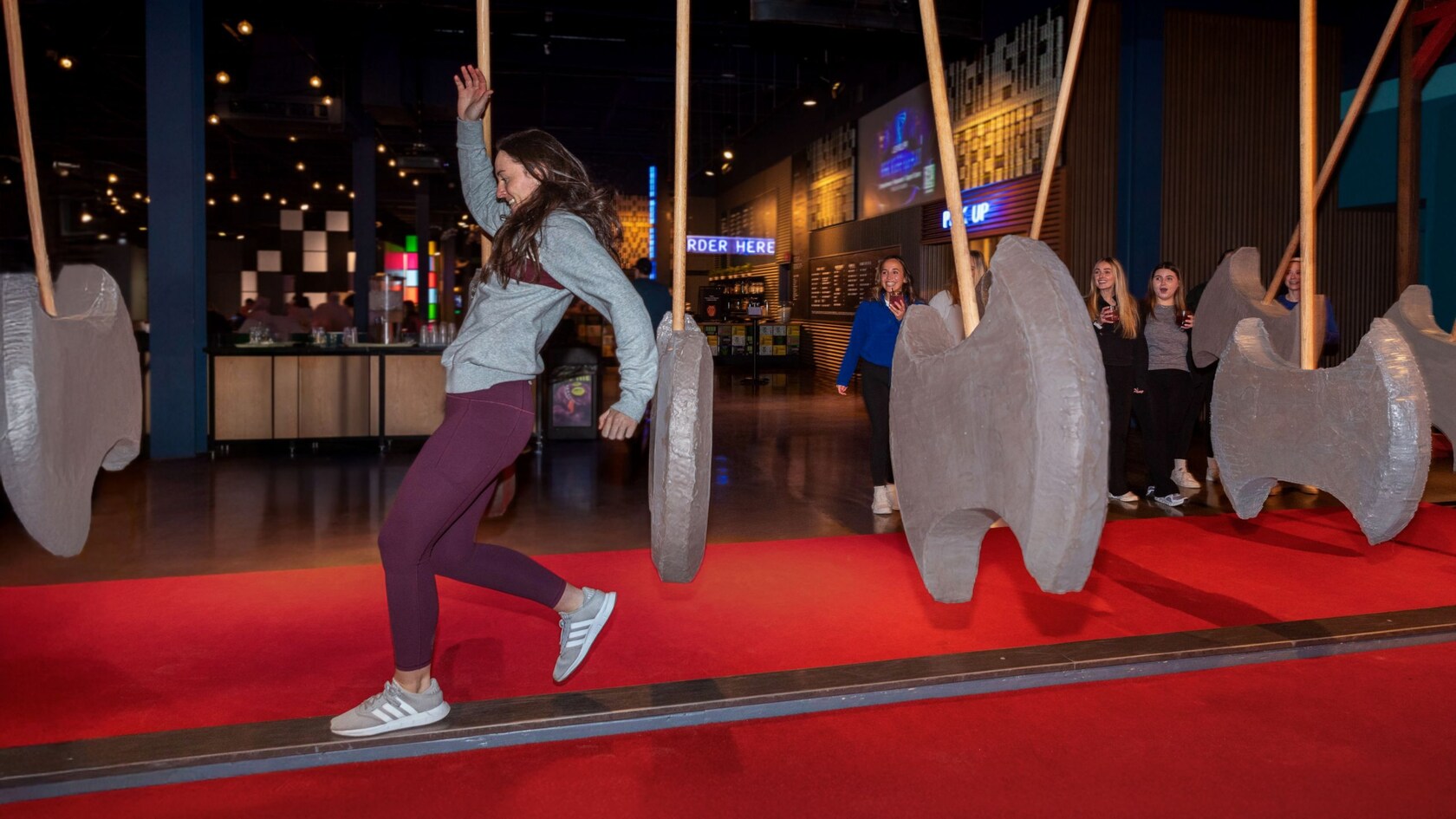 A Guest running on a balance beam through a series of large swinging foam axes